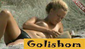 Одинокая нудистка читает книгу на пляже